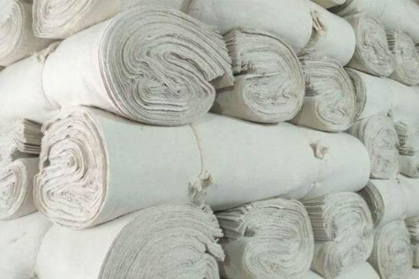 Stacks of tightly rolled white fabric, piled together in a textile warehouse or storage area